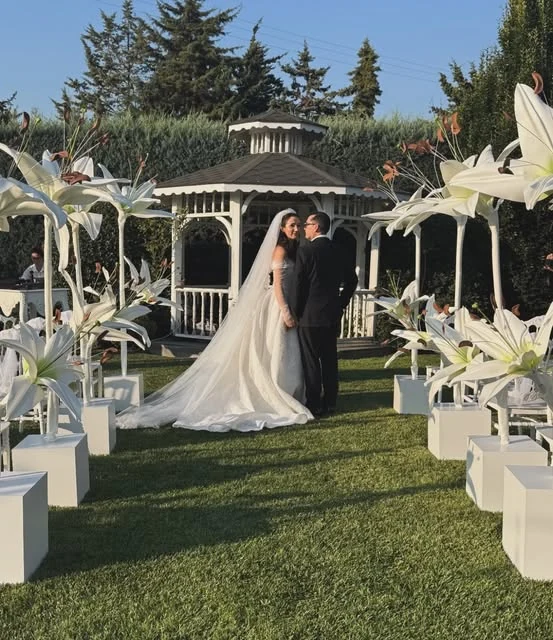 Bahçe düğününde gelin ve damat, çevrelerinde dev beyaz lilyum çiçekleri
